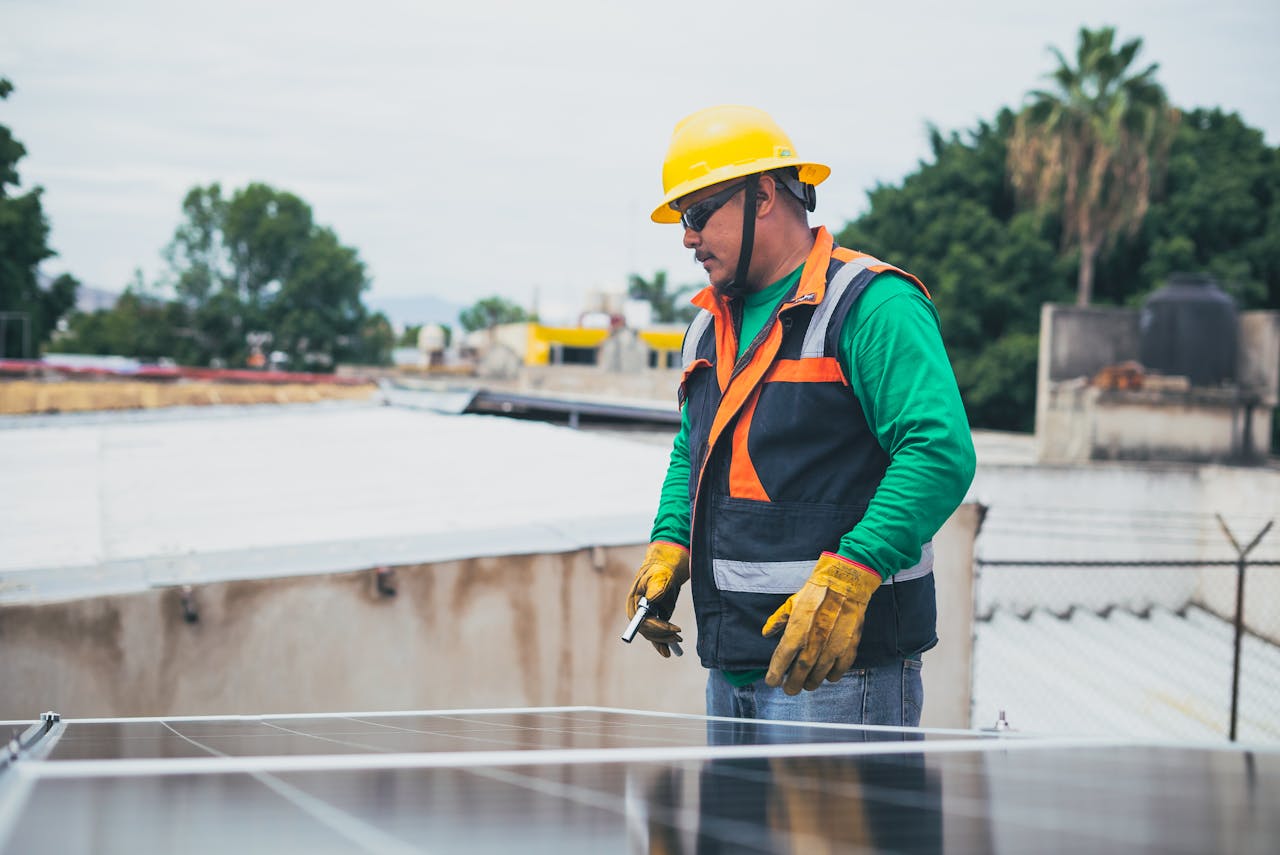 Solar technician inspecting rooftop solar panels while wearing safety helmet and protective gloves.
